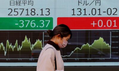 A woman walks past an electric board showing Nikkei index and exchange rate between Japanese Yen and U.S. dollar outside a brokerage at a business district in Tokyo