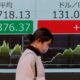 A woman walks past an electric board showing Nikkei index and exchange rate between Japanese Yen and U.S. dollar outside a brokerage at a business district in Tokyo