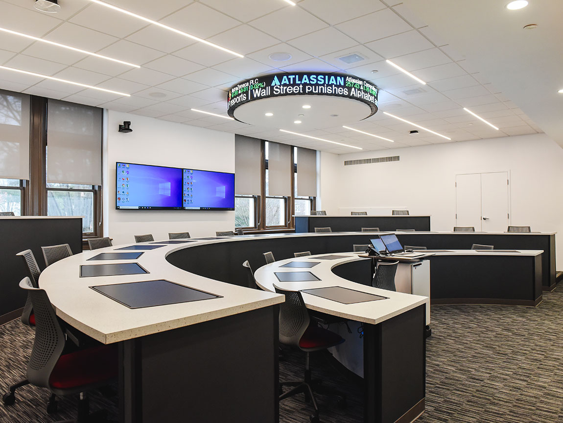 An empty classroom with stadium seats, big screens in the back and a stock quote on the ceiling
