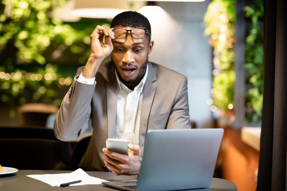 An investor takes off his glasses while looking at his phone in surprise