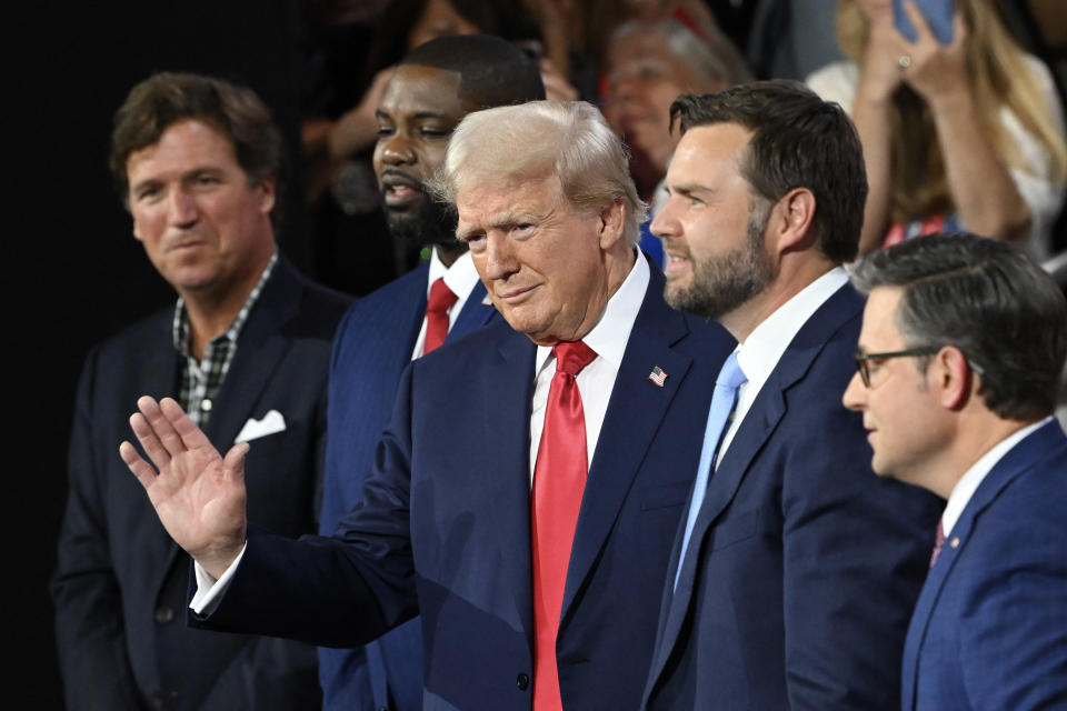 Former U.S. President and 2024 Republican presidential candidate Donald Trump waves as he arrives at his seat during the first day of the 2024 Republican National Convention at Fiserv Forum in Milwaukee, Wisconsin, July 15, 2024. Also pictured (L-R) are U.S. political commentator Tucker Carlson, U.S. Representative from Florida Byron Donalds, U.S. Senator from Ohio and Republican vice presidential candidate J.D. Vance and U.S. House Speaker Mike Johnson. Donald Trump won the formal nomination as the Republican presidential candidate and chose a right-wing loyalist as his running mate, kicking off a triumphalist party convention following last weekend's failed assassination attempt. (Photo by ANDREW CABALLERO-REYNOLDS/AFP) (Photo by ANDREW CABALLERO-REYNOLDS/AFP via Getty Images)